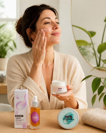 Mujer aplicándose crema facial junto a la crema SHINE, el sérum MILD y el desodorante SILVER BREEZE de BANBU