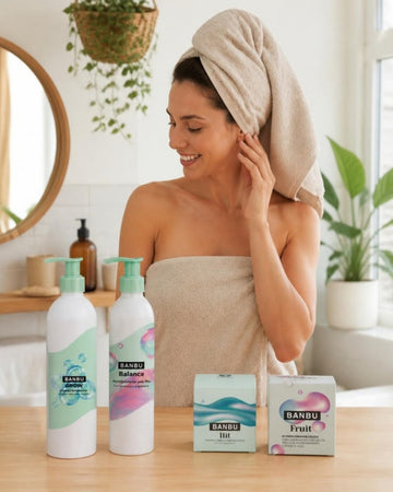 Mujer con toalla en el pelo junto al champú GROW, el acondicionador BALANCE, el champú sólido HIT y el acondicionador sólido FRUIT de BANBU