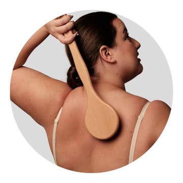 Modelo usando un bath brush para limpiar su espalda, disfrutando de una exfoliación corporal suave y natural.