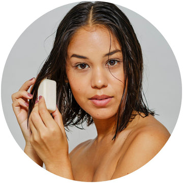 Chica con el cabello húmedo sosteniendo un acondicionador sólido natural, lista para nutrir y suavizar su melena de forma sostenible.