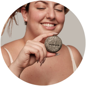 Chica con una toalla en el pelo sosteniendo un champú sólido natural, lista para un cuidado capilar sin residuos y libre de tóxicos.