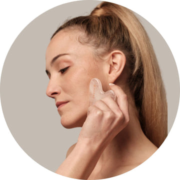Chica aplicándose una gua sha en el rostro, masajeando suavemente la piel para estimular la circulación y mejorar la firmeza. Ideal para el cuidado facial natural