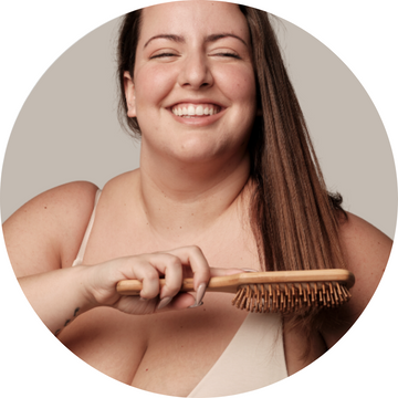 Chica peinándose con un cepillo de madera natural, disfrutando de un cuidado capilar suave y sostenible