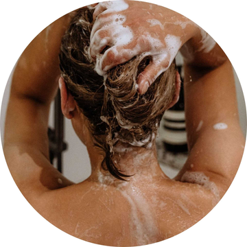 Mujer aplicándose champú natural sin sulfatos, siliconas ni parabenos, con espuma en el cabello