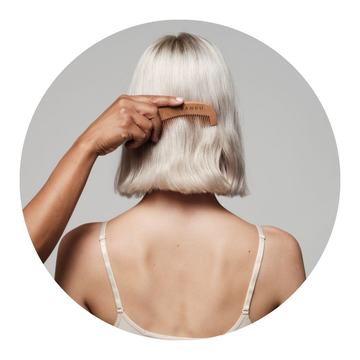 Chica con el cabello corto peinándose con un cepillo de madera natural que pertenece a la categoría de accesorios capilares, cuidando su melena de manera sostenible