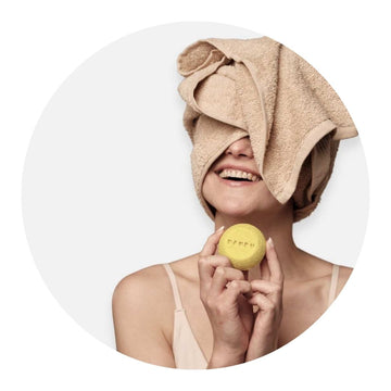 Chica con la toalla en la cabeza mientras sujeta un champú sólido de la colección de cosmética ecológica