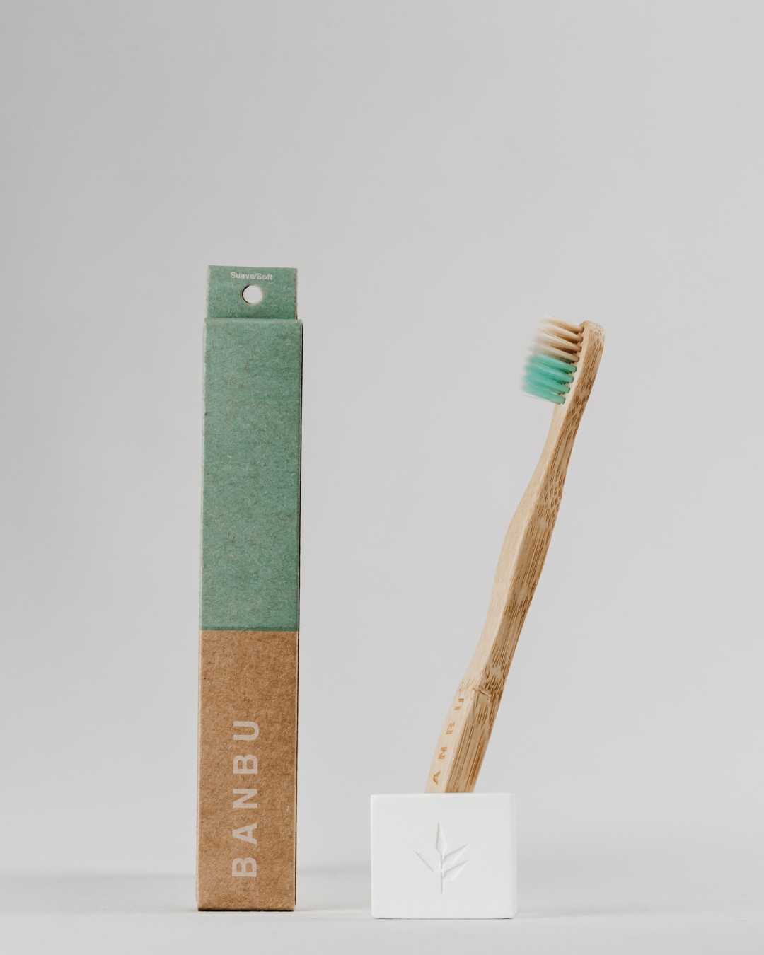 Fotografía de producto de un cepillo de dientes para bebés y niños de la marca BANBU, elaborado con mango de bambú moso y cerdas suaves de color verde y beige, colocado junto a su caja de empaque de cartón ecológico libre de plástico.