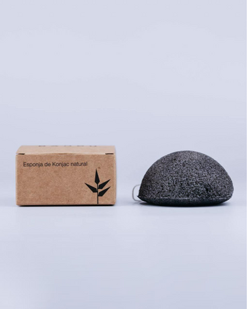 Esponja facial konjac con carbón activado junto a la caja en la que viene para su transporte.