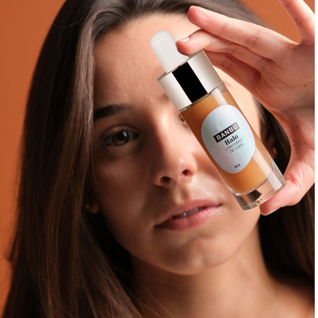 Mujer sujetando el contorno de ojos ecológico HALO de Banbu, mirándolo con atención, destacando su interés en los beneficios naturales del producto para el cuidado ocular