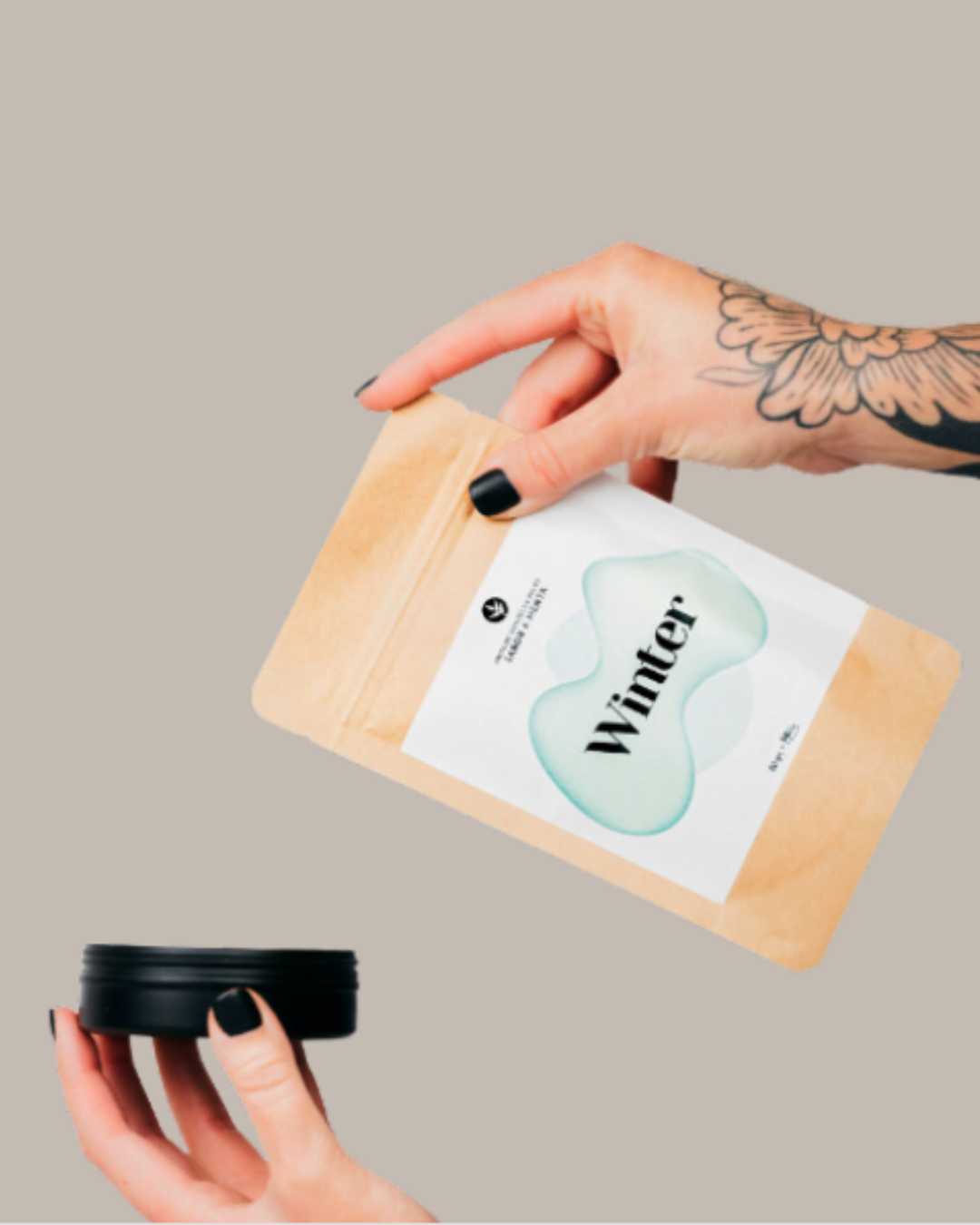 Manos sosteniendo el sobre kraft de recarga de pasta de dientes Winter sabor menta junto a una lata de aluminio negra.